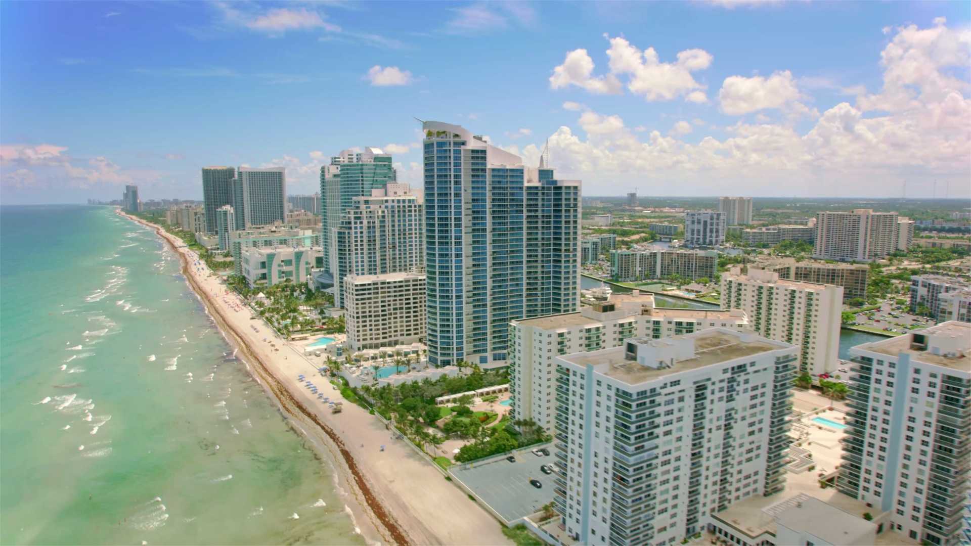 aerial view of a series of multifamily high rise buildings on a coastline with a beach and breaking waves